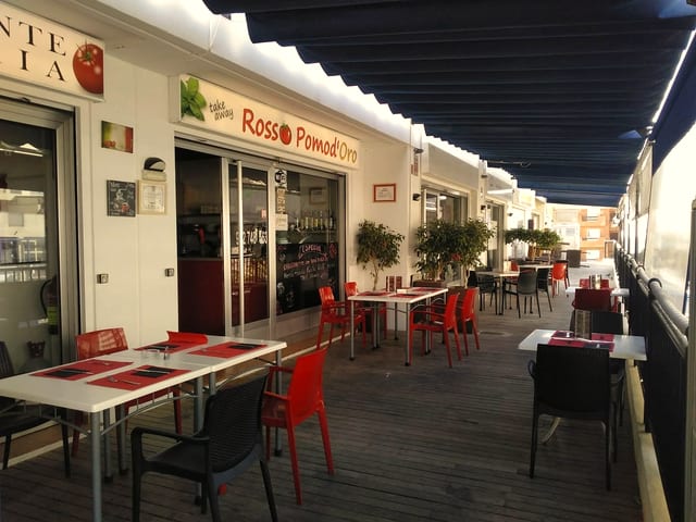 Fachada del local con el rótulo Rosso Pomod'Oro y mesas con mantel rojo en la terraza